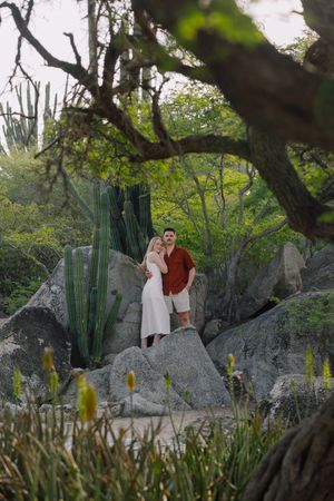 Couple standing on rocks surrounded by cacti and lush greenery in a scenic desert garden setting.