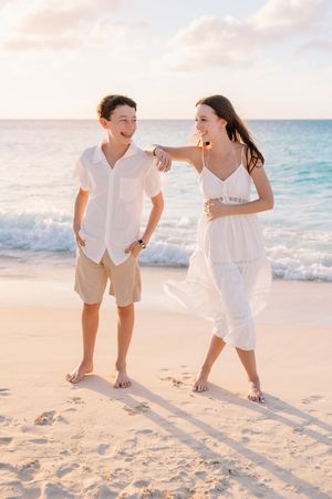 Family members walking and laughing together along a pristine beach at sunset.