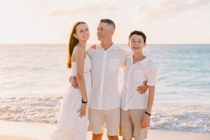 Family dressed in white and beige enjoying a beach photoshoot at sunset.