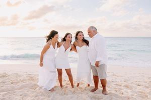 Family of four in white outfits laughing together on a tropical beach at sunset.