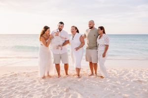Family walking together on a white sandy beach at sunset with ocean waves in the background.