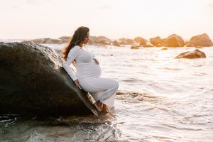 Person sitting on coastal rocks during sunset with ocean waves crashing below.