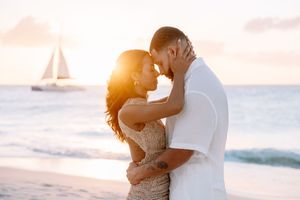 Romantic beach embrace with sailboat silhouette in golden sunset background.