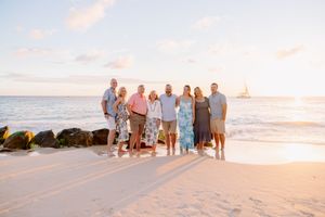 Large family gathering on beach at sunset with ocean and rocks in background.