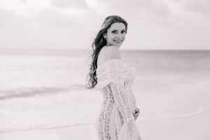 Woman in white lace dress posing on beach with soft overcast lighting.