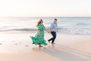 Couple in coordinated outfits walking and dancing on beach at golden hour.