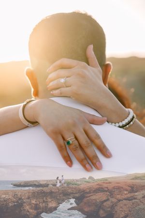 Close up of hands with rings against a scenic coastal cliff backdrop at sunset.