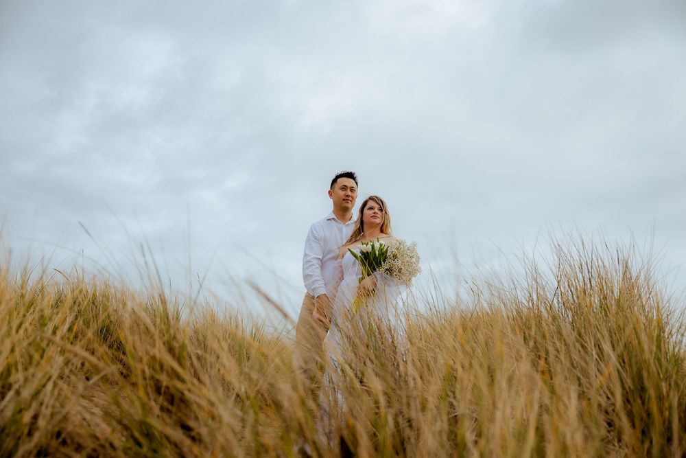 Romantic couple embracing in tall coastal grass during sunset.