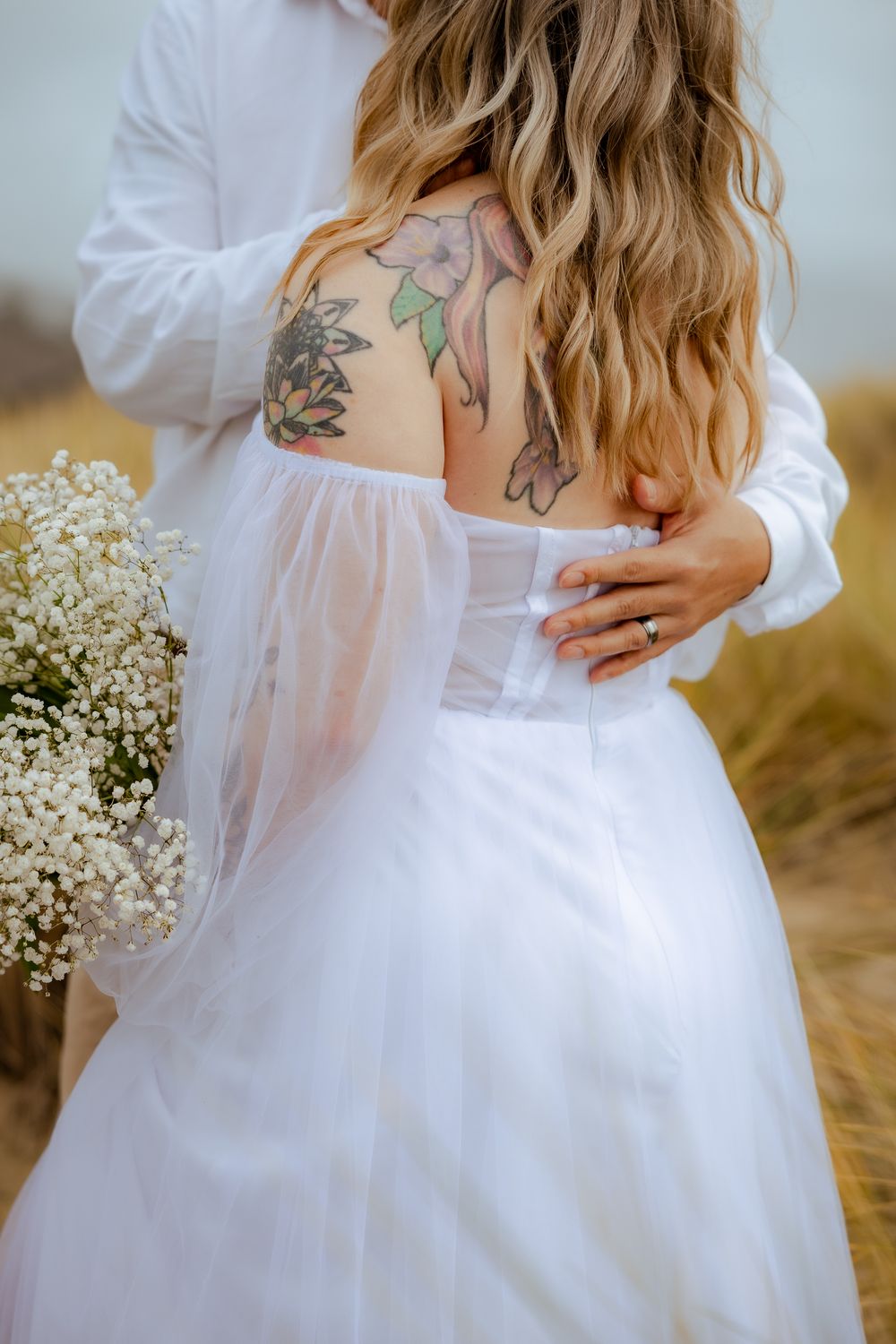 Close-up of couple embracing showing white dress details and floral bouquet.
