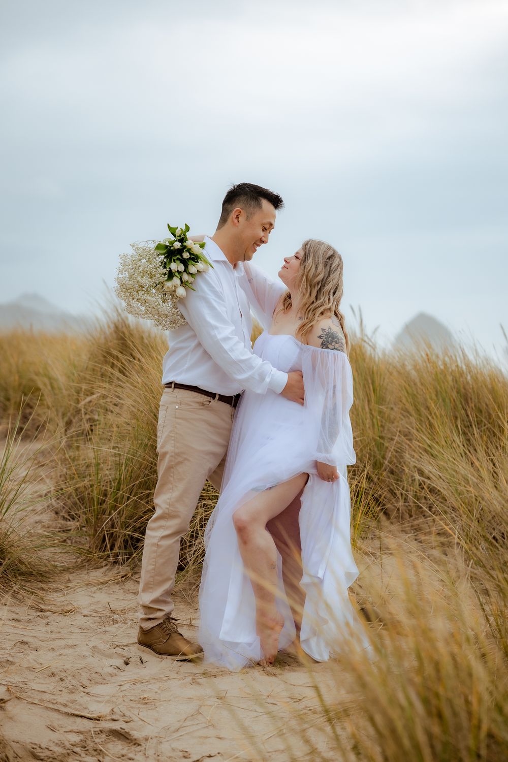 Couple in white clothing sharing romantic moment on sandy dunes.