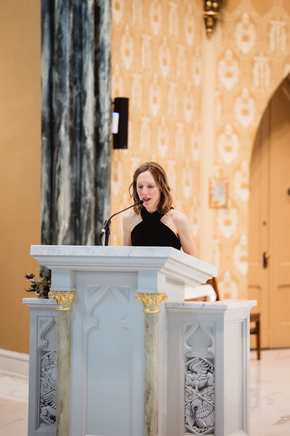 White decorative podium with ornate details stands against a peach-colored patterned wallpaper in an elegant venue setting.
