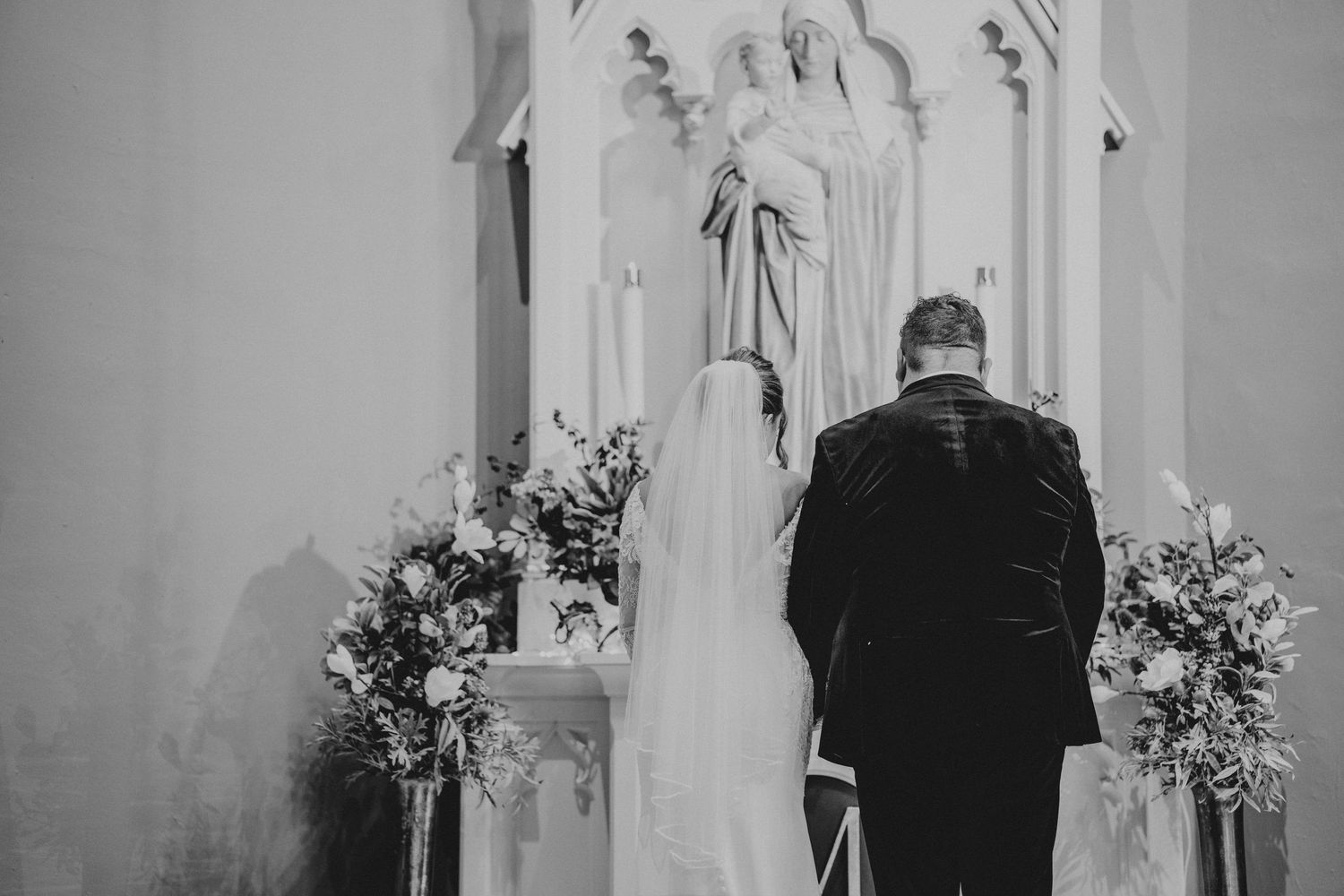 A black and white photo of a church altar decorated with floral arrangements during a wedding ceremony.