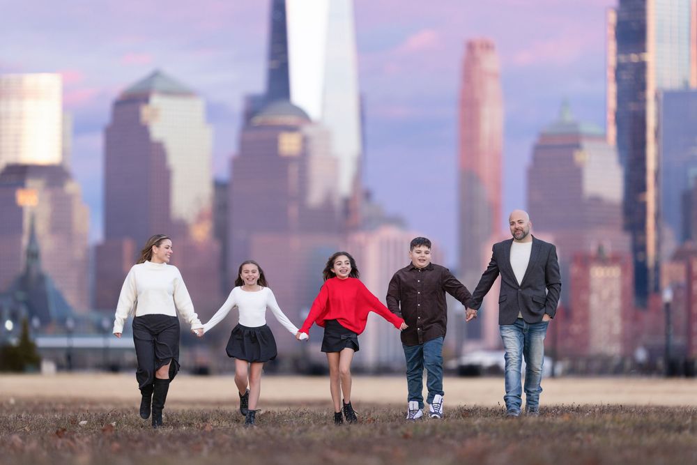 Family holding hands walking together with NYC skyline backdrop at dusk.