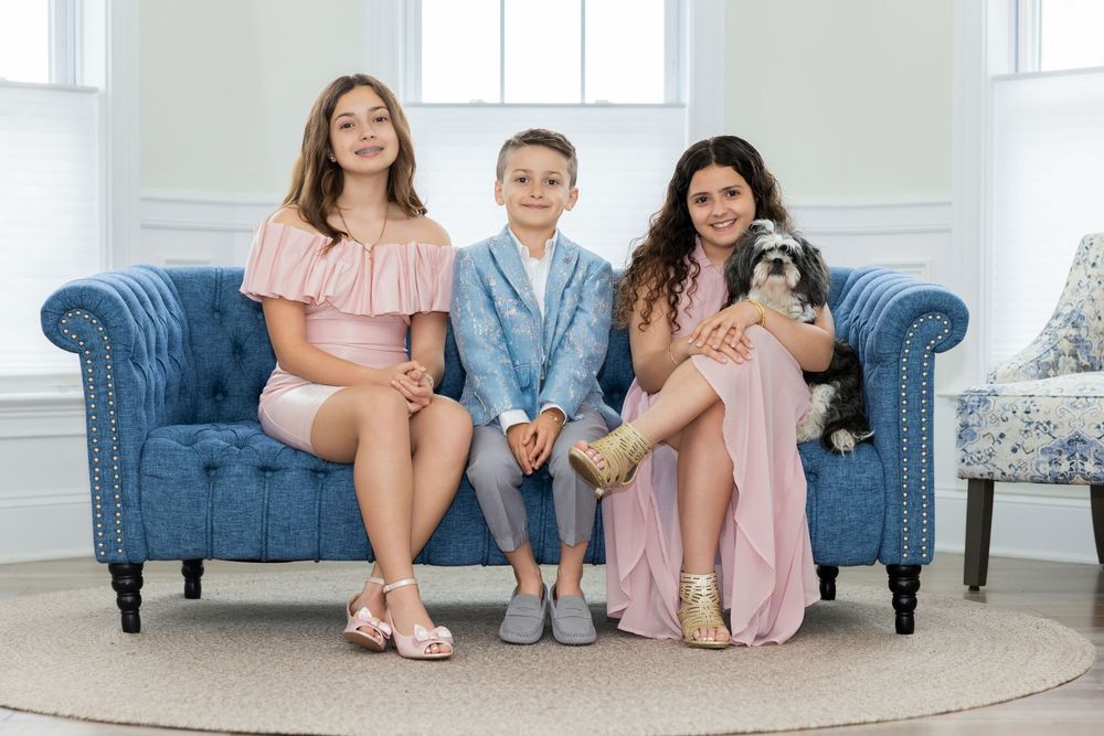 Three children and woman in pink outfits sitting on blue couch with small dog.