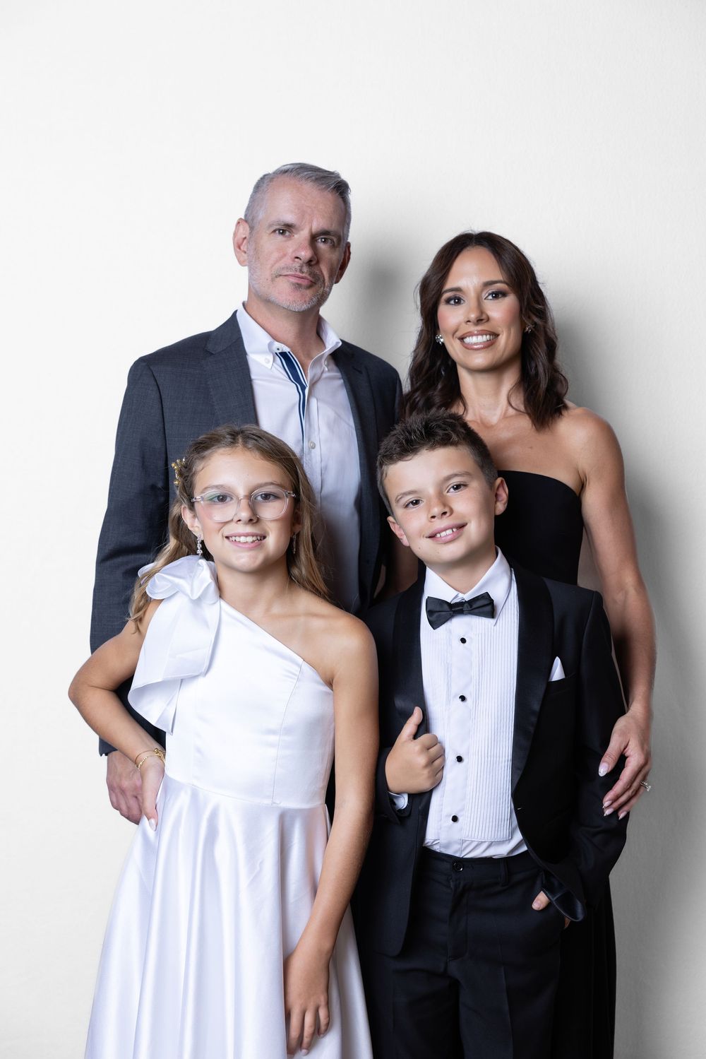 Formal family portrait with parents and two children dressed in elegant black and white attire against light background.