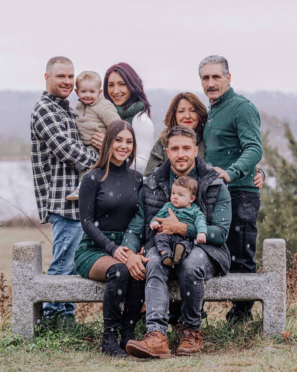 Family sitting together on stone wall during outdoor photo session in casual winter attire.
