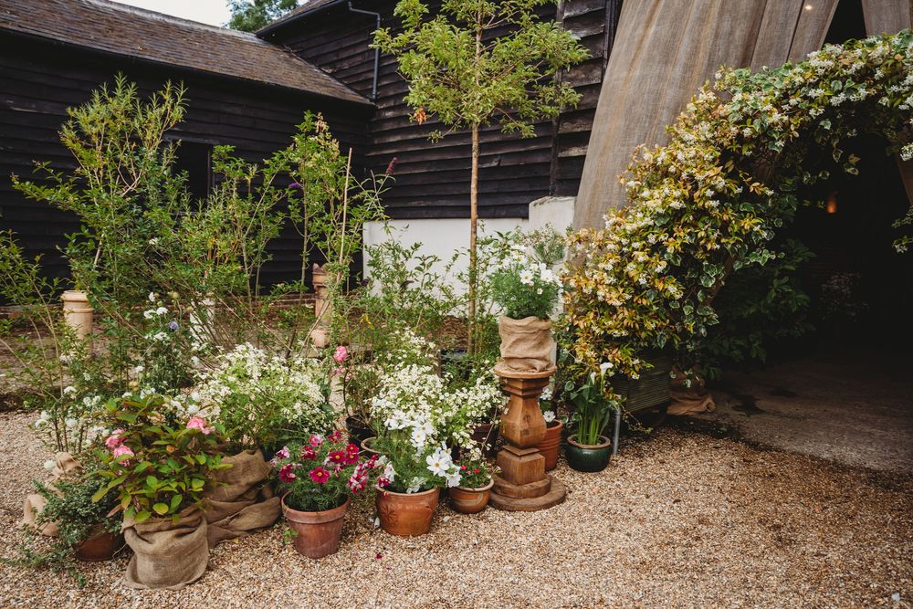 A rustic barn venue with potted plants and gravel path creates a charming wedding setting.