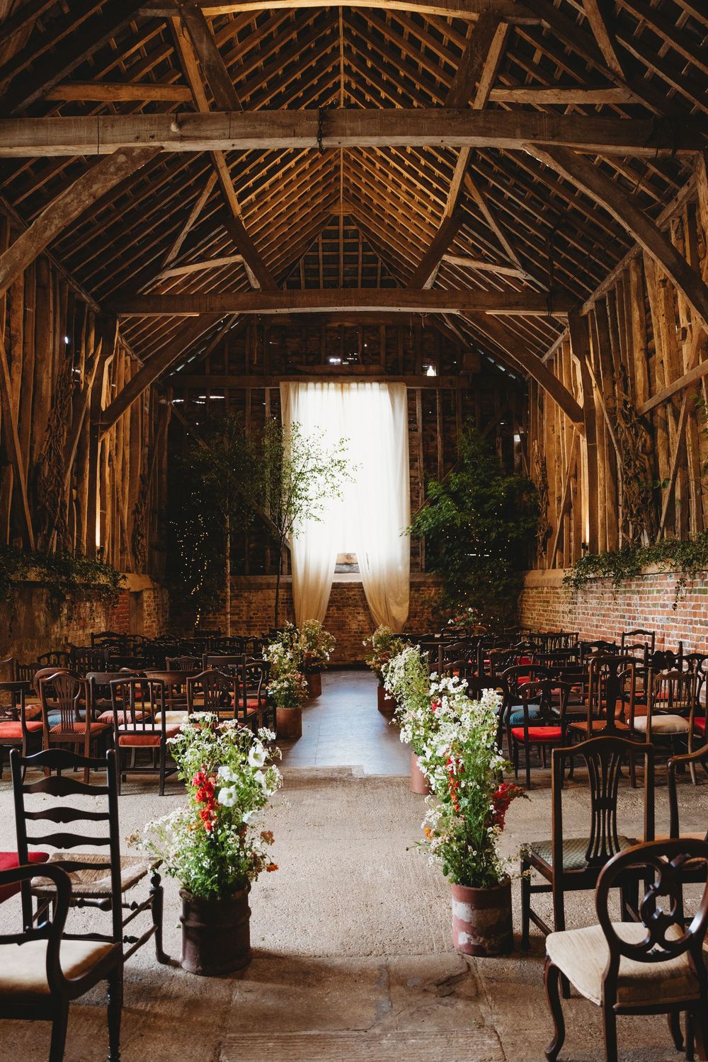 Rustic barn wedding venue with exposed wooden beams and rows of chairs decorated with floral arrangements.