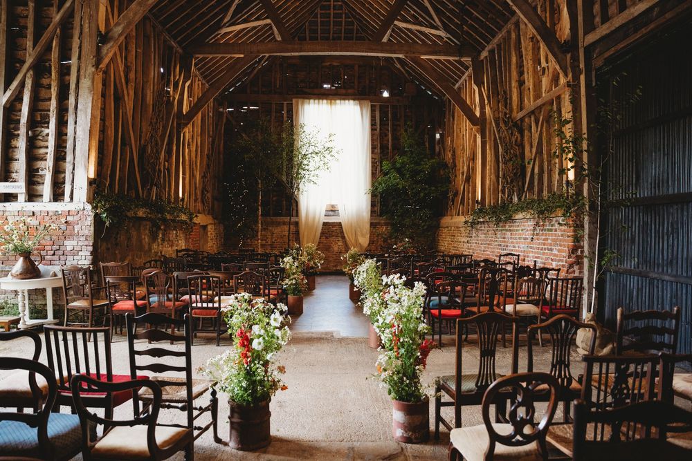 Interior of a historic barn set up for a wedding ceremony with dark wooden chairs and natural lighting.