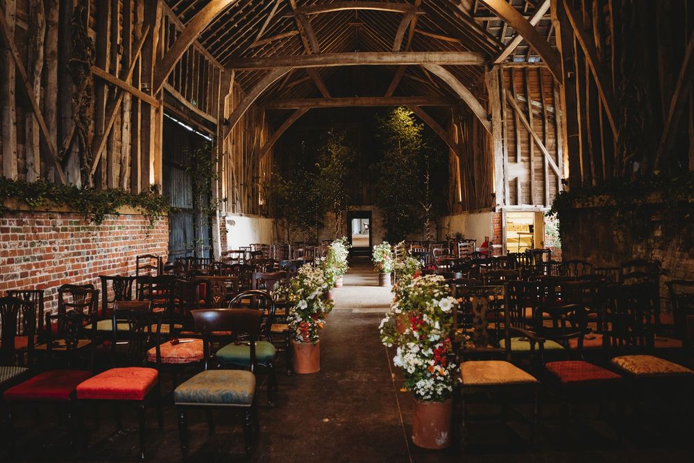 Atmospheric barn wedding setup with vintage chairs and romantic lighting streaming through windows.