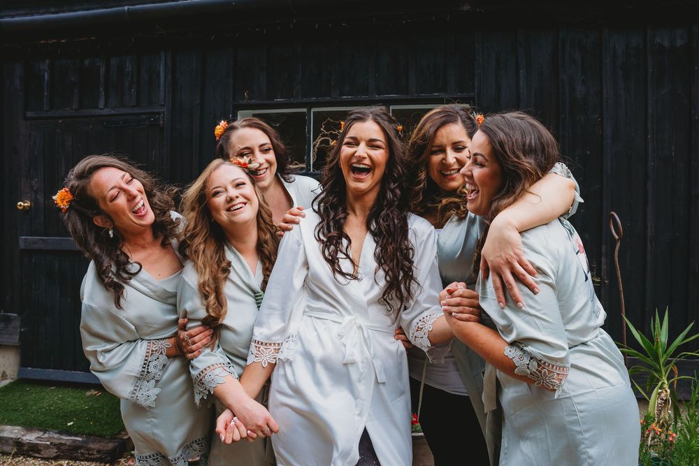 Group of bridesmaids in white robes sharing a joyful moment together.