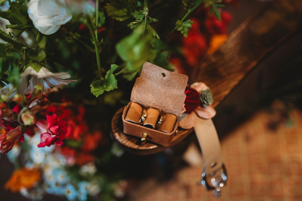 Brown leather wedding ring box nestled among colorful floral arrangements.