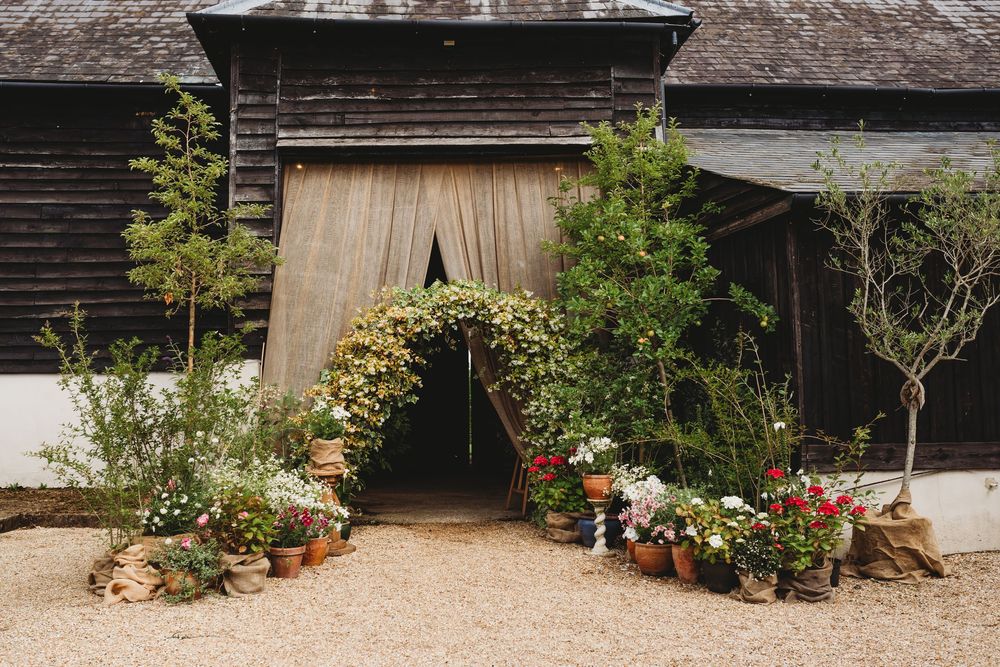 Rustic barn entrance decorated with floral arch and potted plants creating a wedding venue.