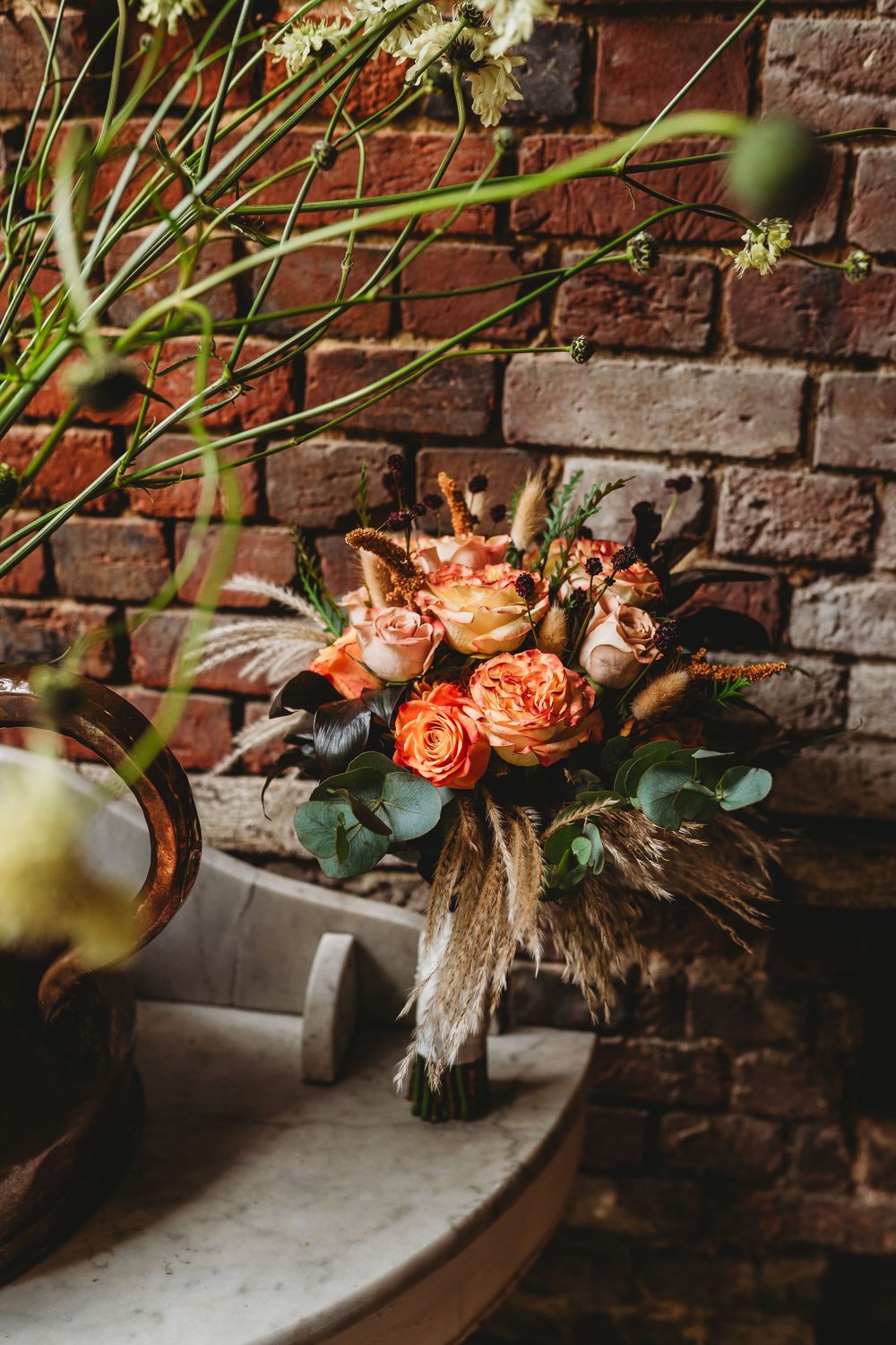Peach-colored roses and greenery bouquet arranged against rustic brick wall.