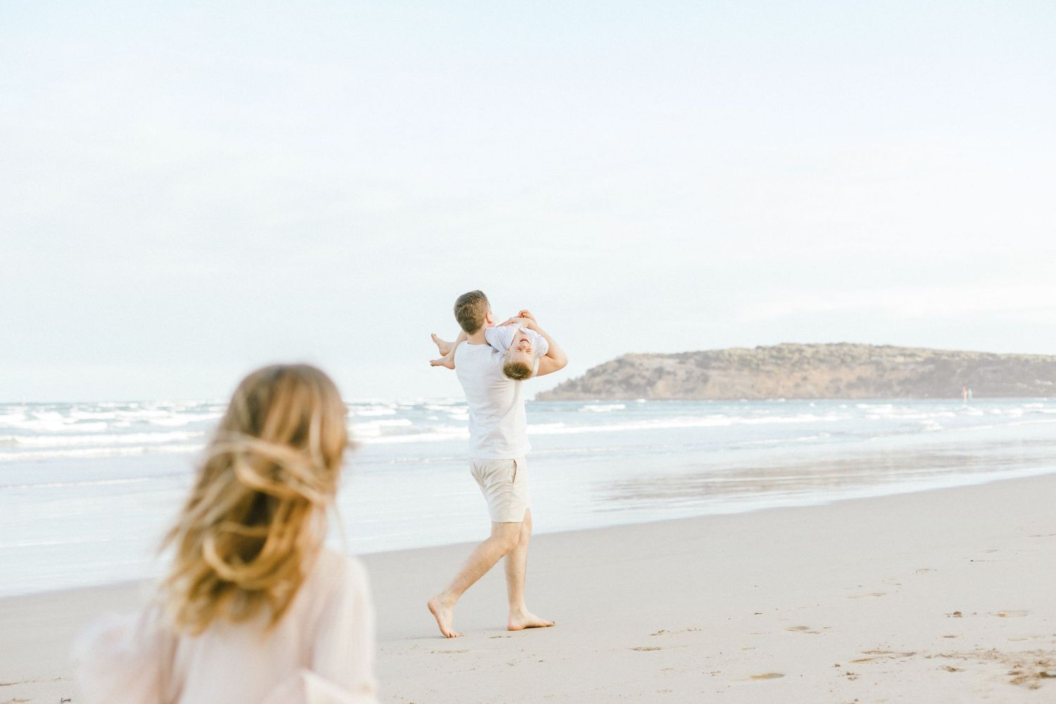 Family walking along sandy beach at sunset with waves crashing in background.