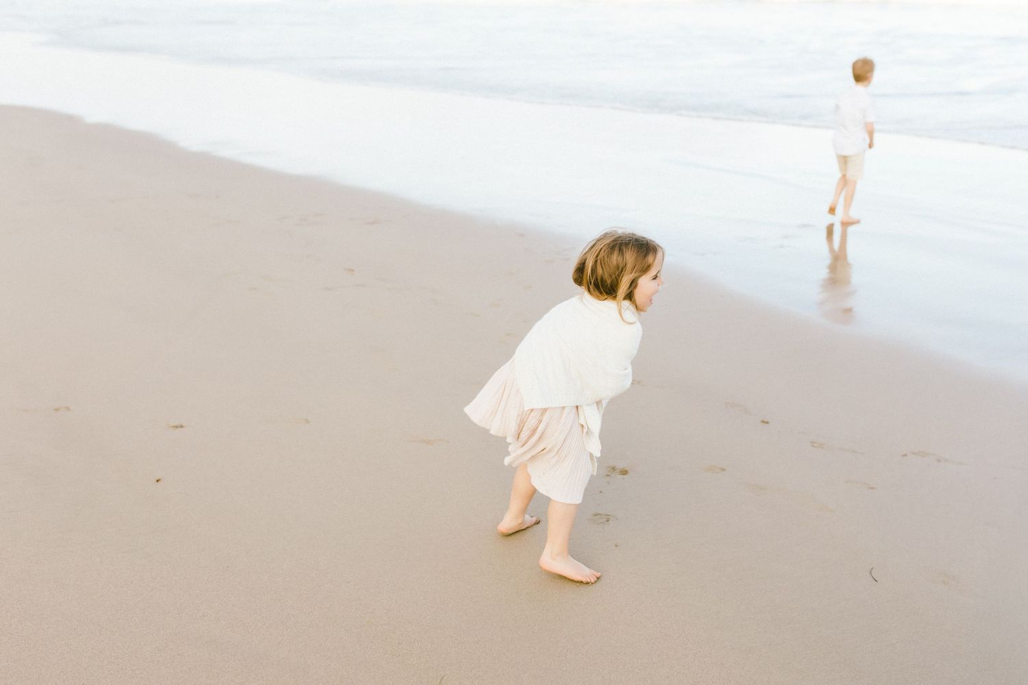 A person in white clothing walks along a misty beach shoreline at dawn creating a peaceful, ethereal scene.