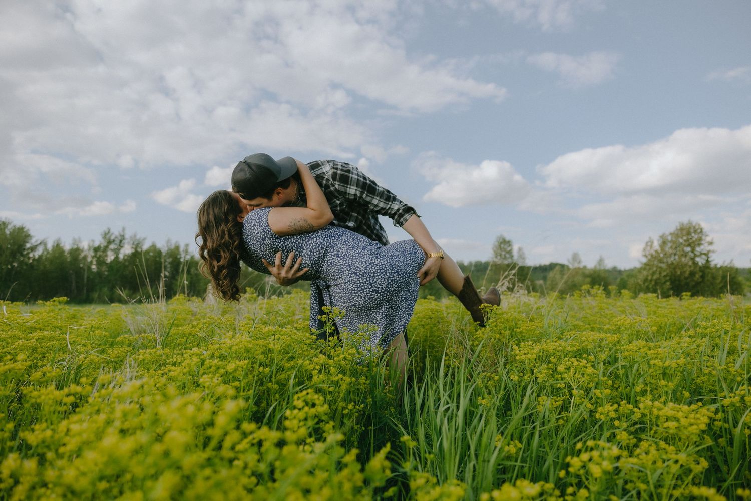 Couple sitting together in a lush green meadow with tall grass and birch trees on a summer day.