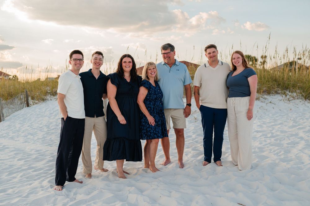 Group of people in coordinated navy and white outfits walking along a pristine white sand beach at sunset.