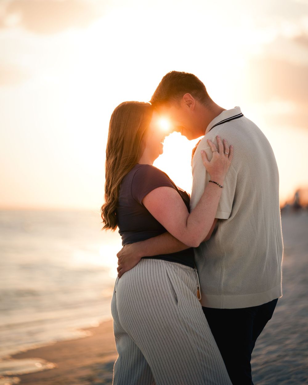 A couple embraces on a beach during a romantic sunset photoshoot, creating silhouettes against the golden sky.