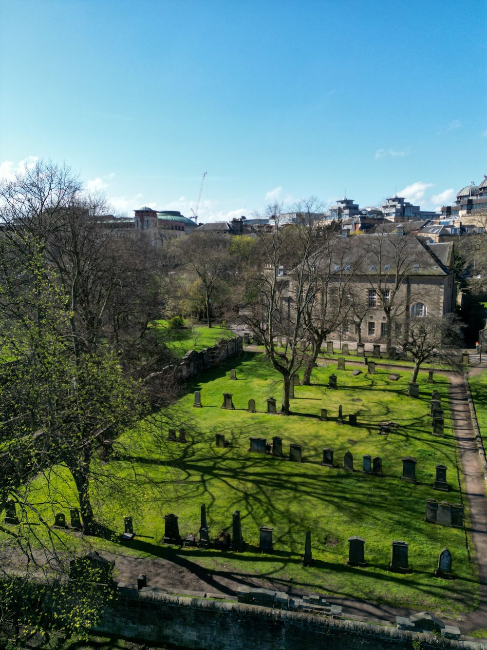 Historic cemetery grounds with green grass and stone buildings visible on a sunny day.