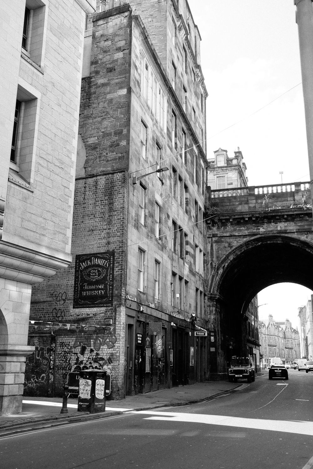 Historic stone buildings line a narrow cobblestone street in Edinburgh's Old Town with an archway visible in the distance.