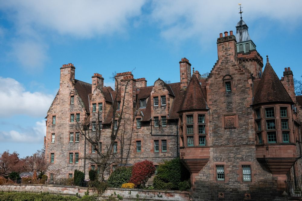 Row of Gothic-style brick buildings with distinctive chimneys and dormers against a blue sky.