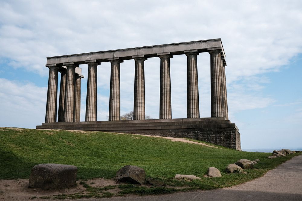 Ancient stone columns stand on a grassy hilltop overlooking a scenic landscape.