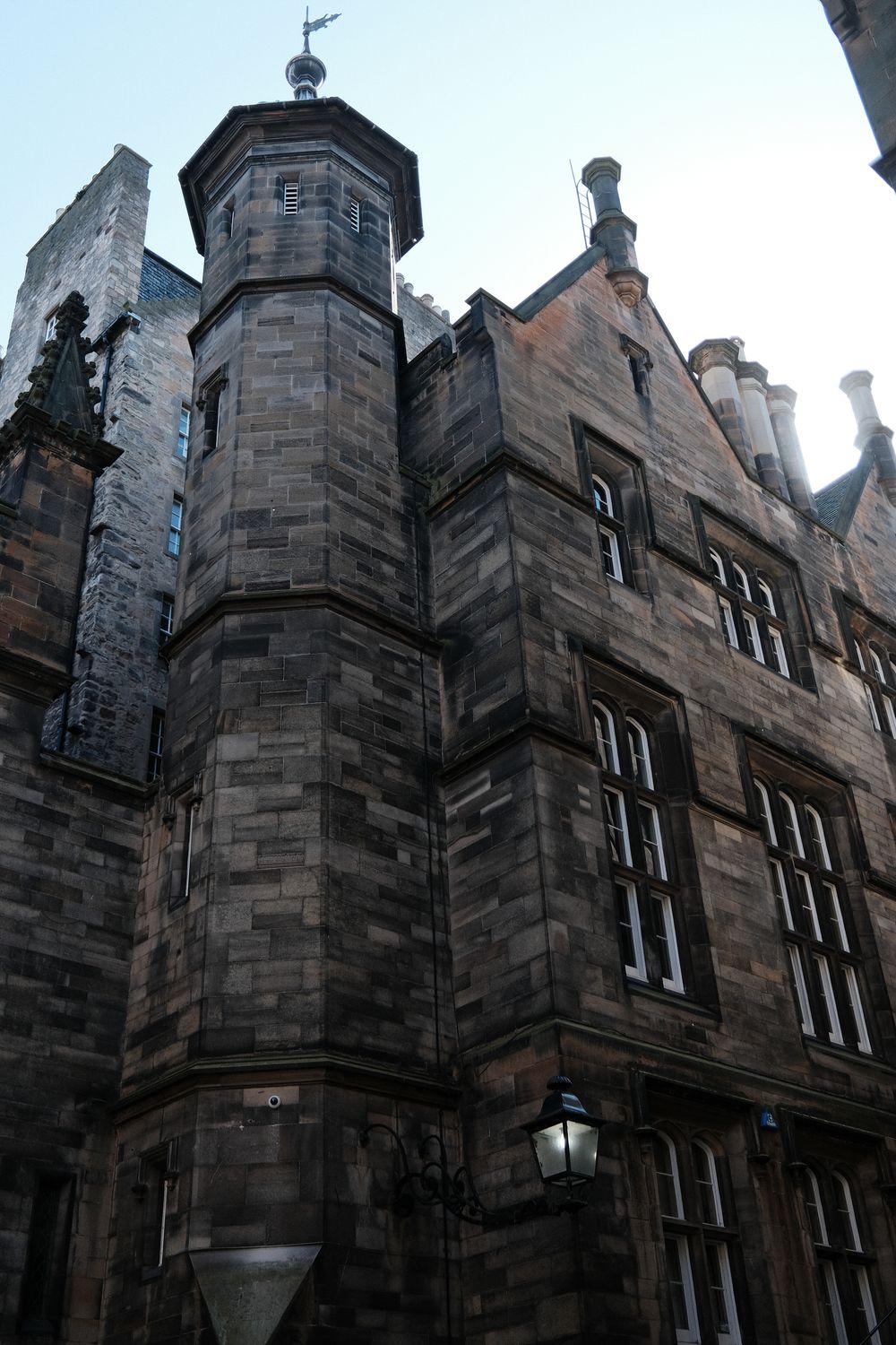 Gothic stone architecture with turret and tall windows on a historic building featuring ornate Victorian details and a lamp.