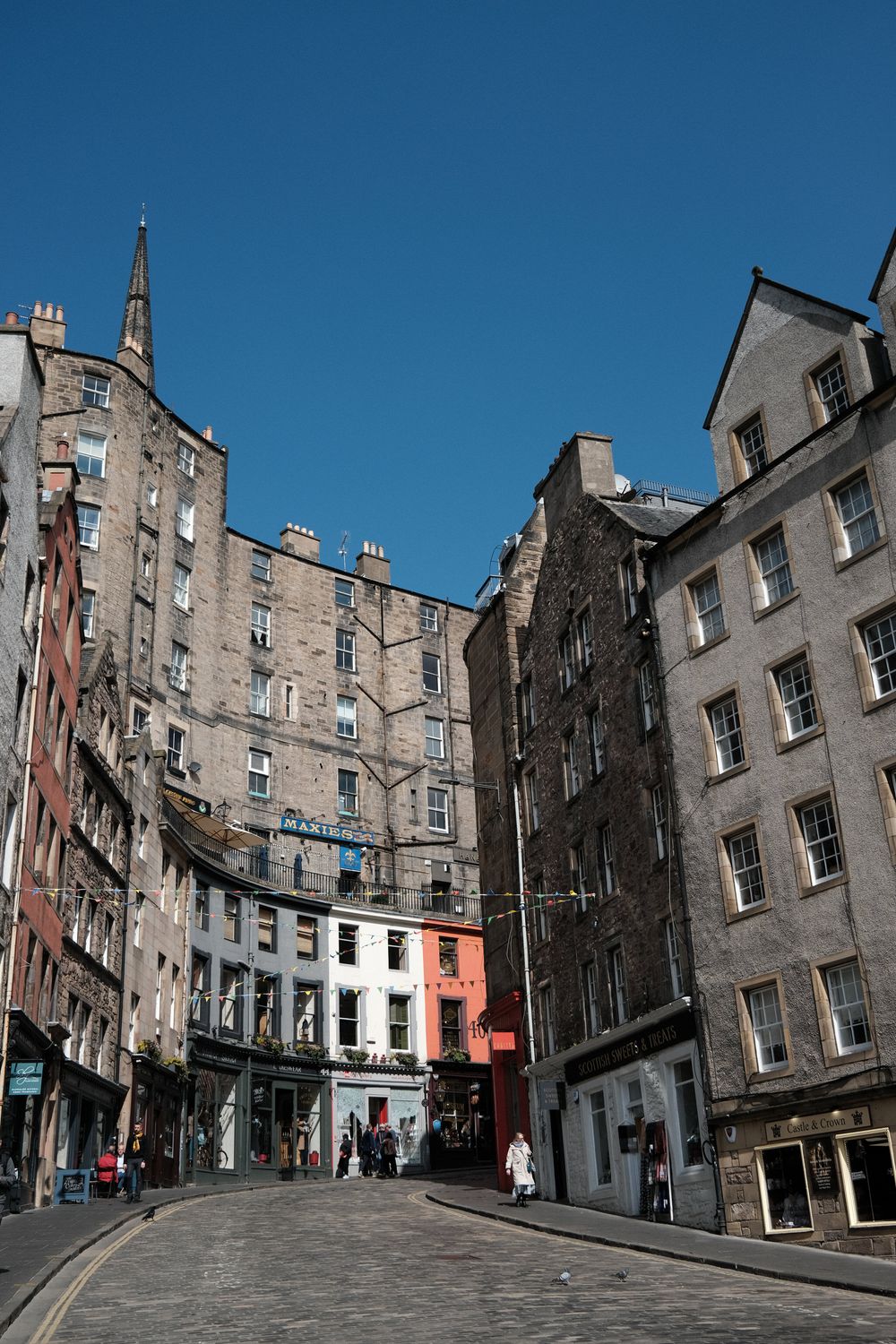 Historic stone buildings line a steep cobblestone street in Edinburgh's Old Town, showcasing traditional Scottish architecture.