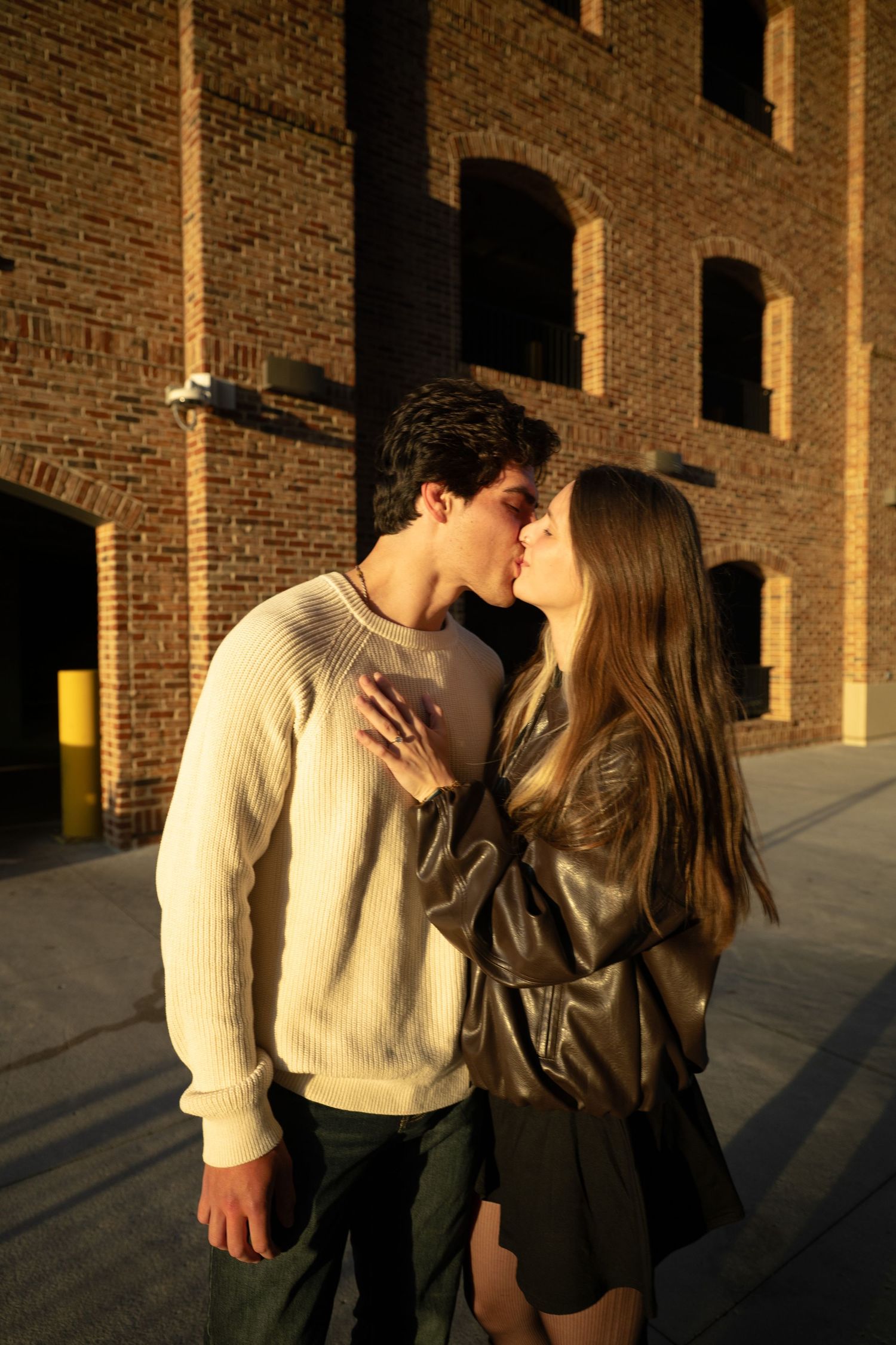 A romantic couple sharing a tender moment at sunset against a brick building backdrop.
