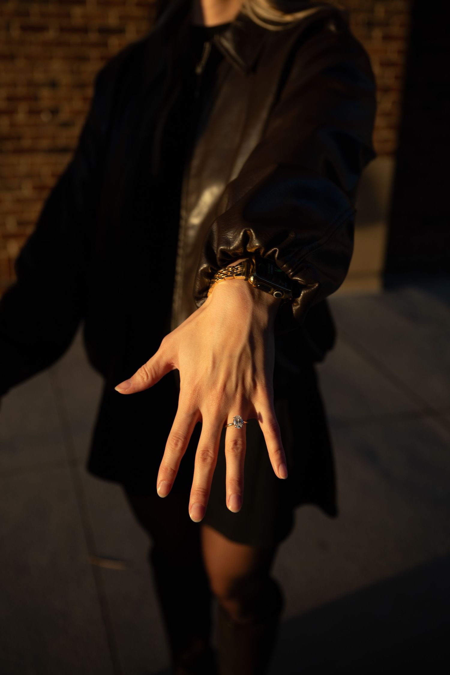 A hand wearing a dark ring casts dramatic shadows against a brick wall in moody lighting.