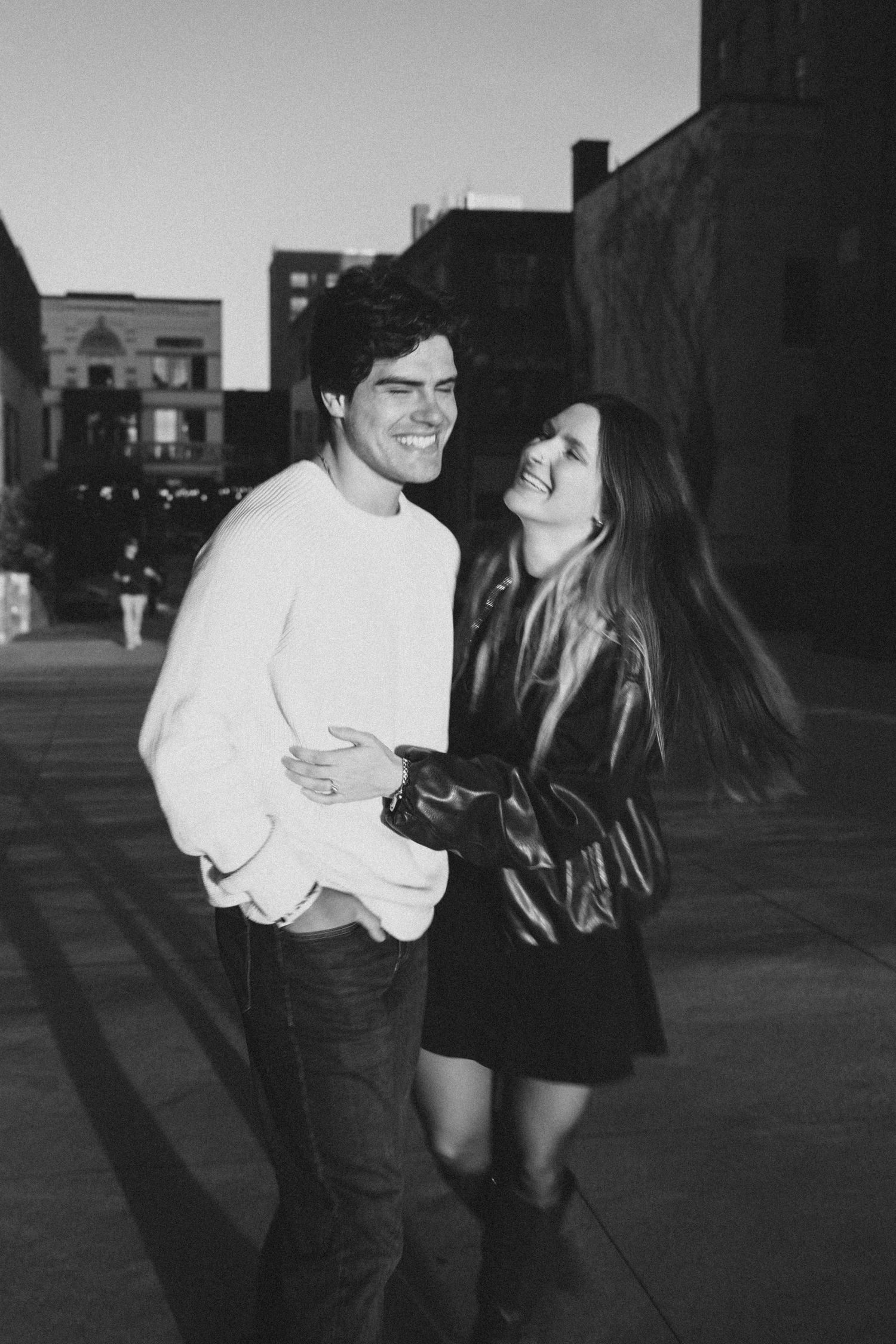 A couple in black and white share an intimate moment on a city street at dusk.