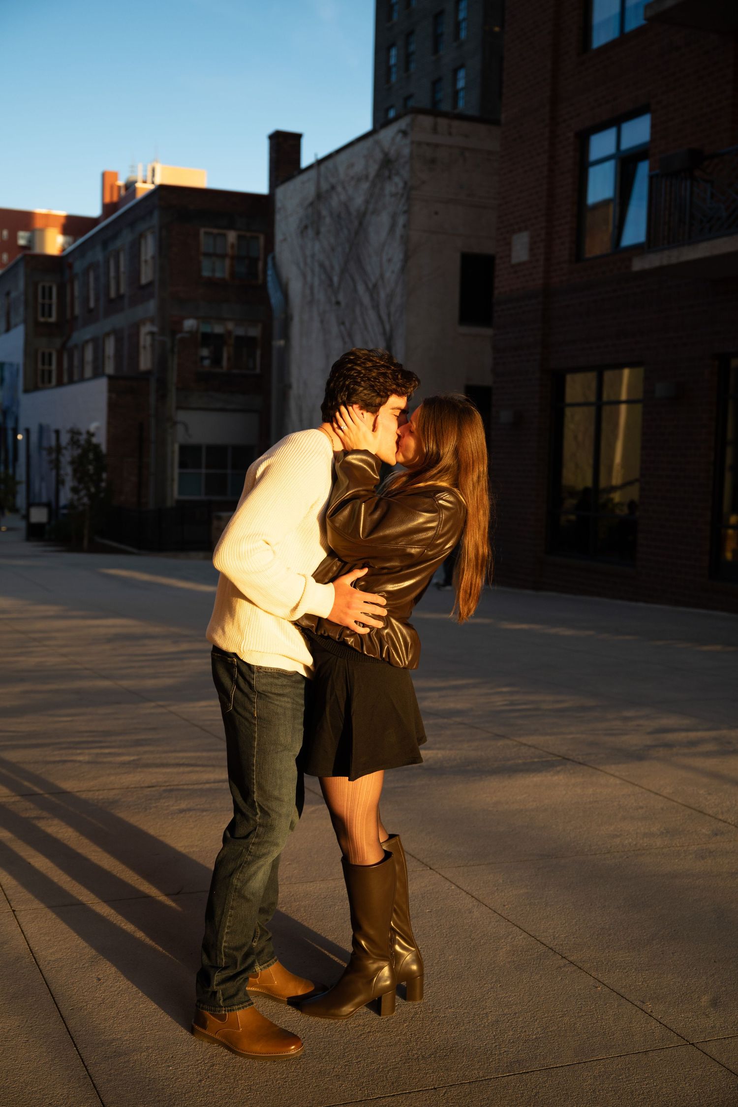 Couple sharing an intimate moment on a city rooftop at dusk with urban buildings in background.