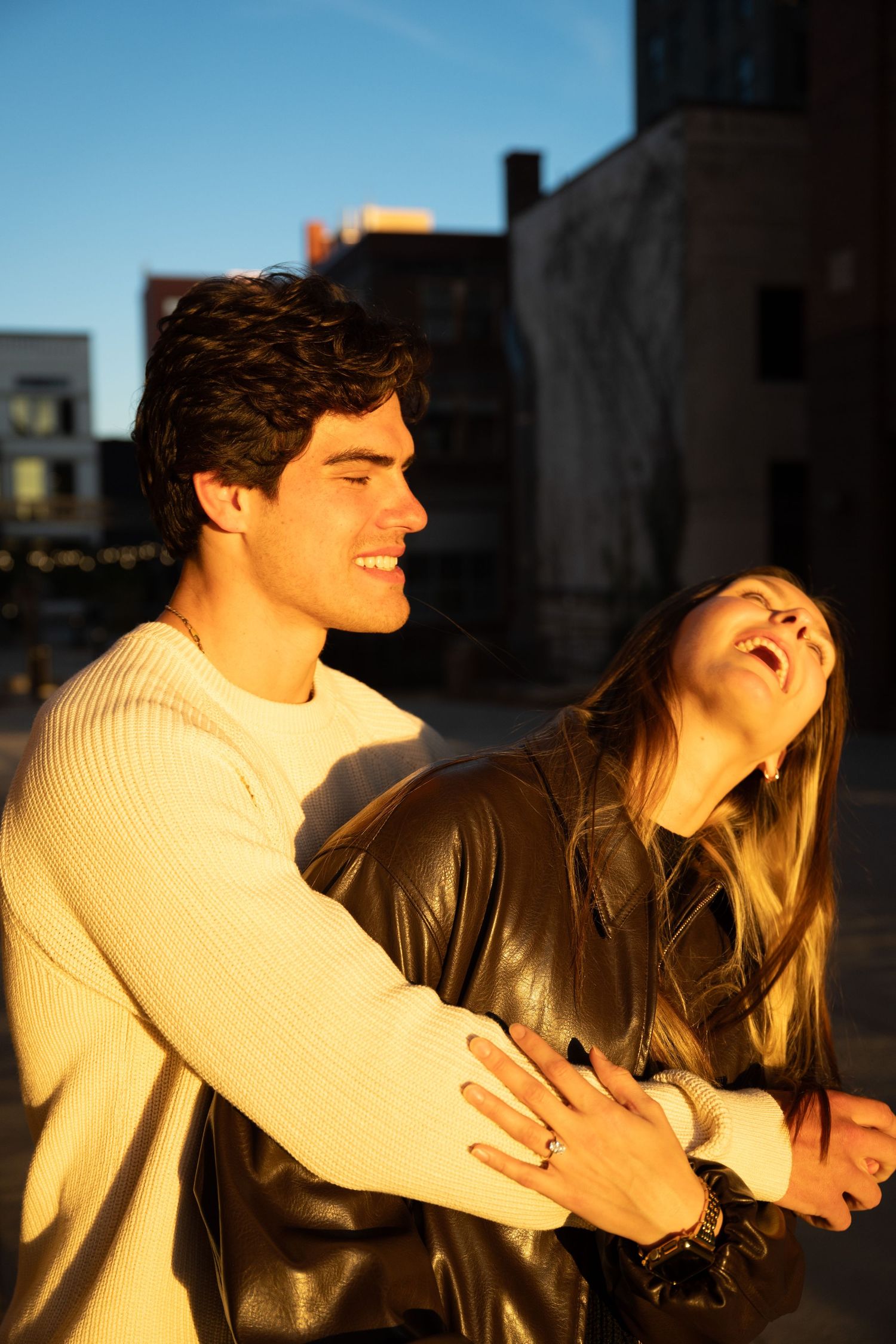 A joyful couple laughing together in golden hour sunlight outside an urban building.