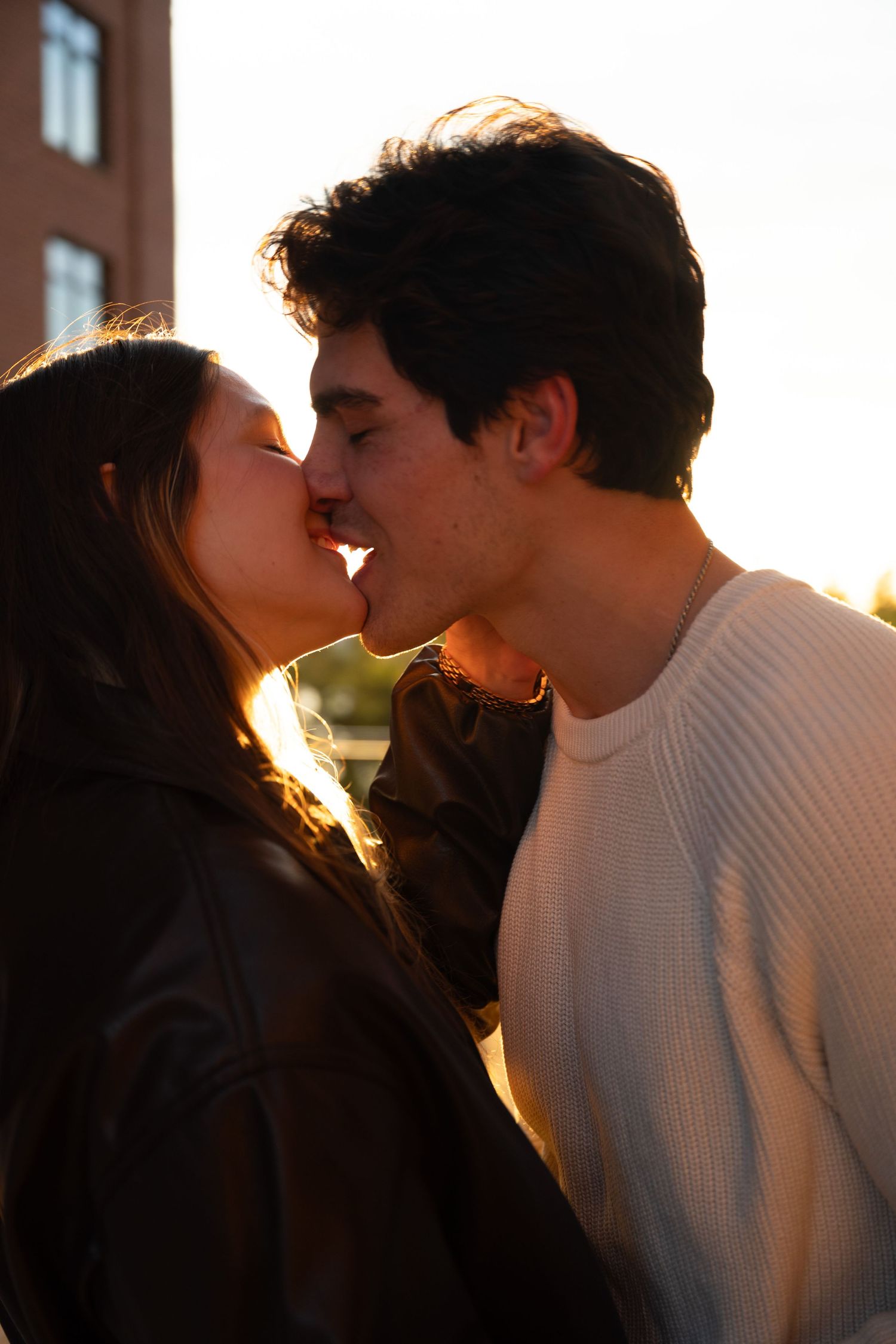 A romantic sunset kiss captured between a couple wearing contrasting light and dark outfits.