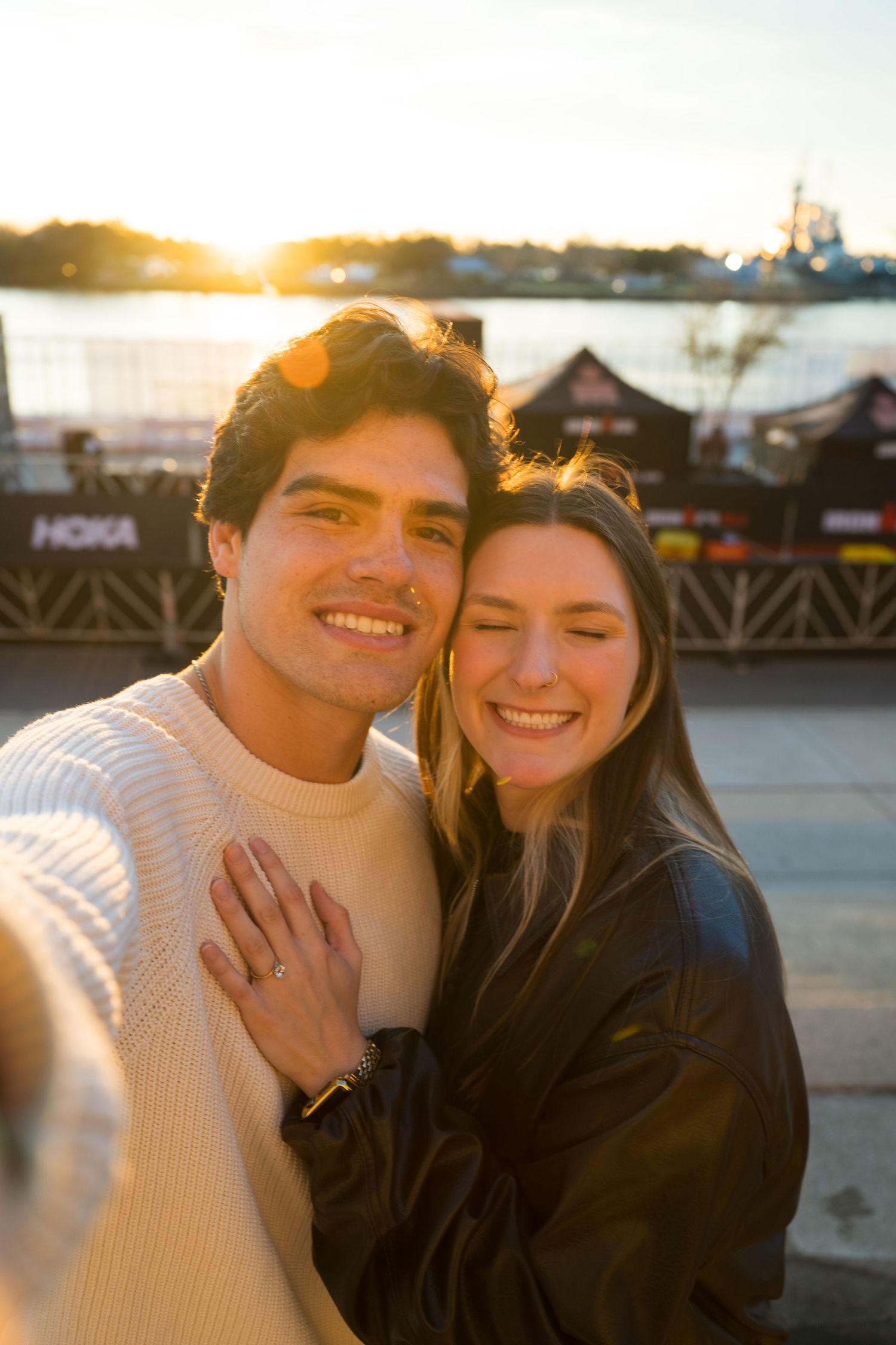 A couple shares a romantic moment at sunset wearing white and black sweaters by the waterfront.