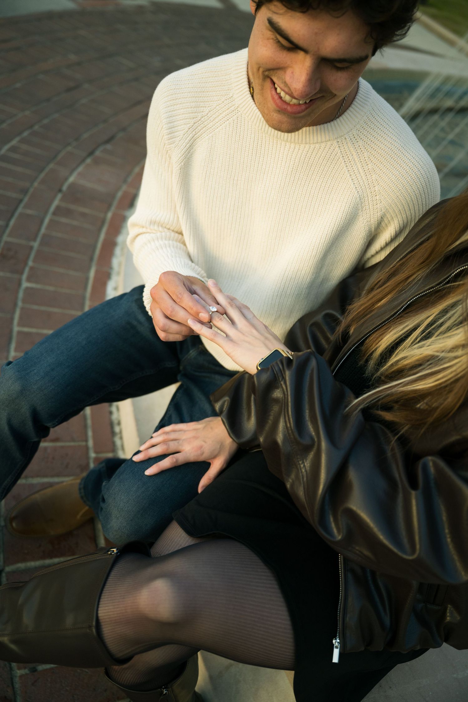 Close-up sequence showing hands wearing a cream sweater and dark pants against a brick background.