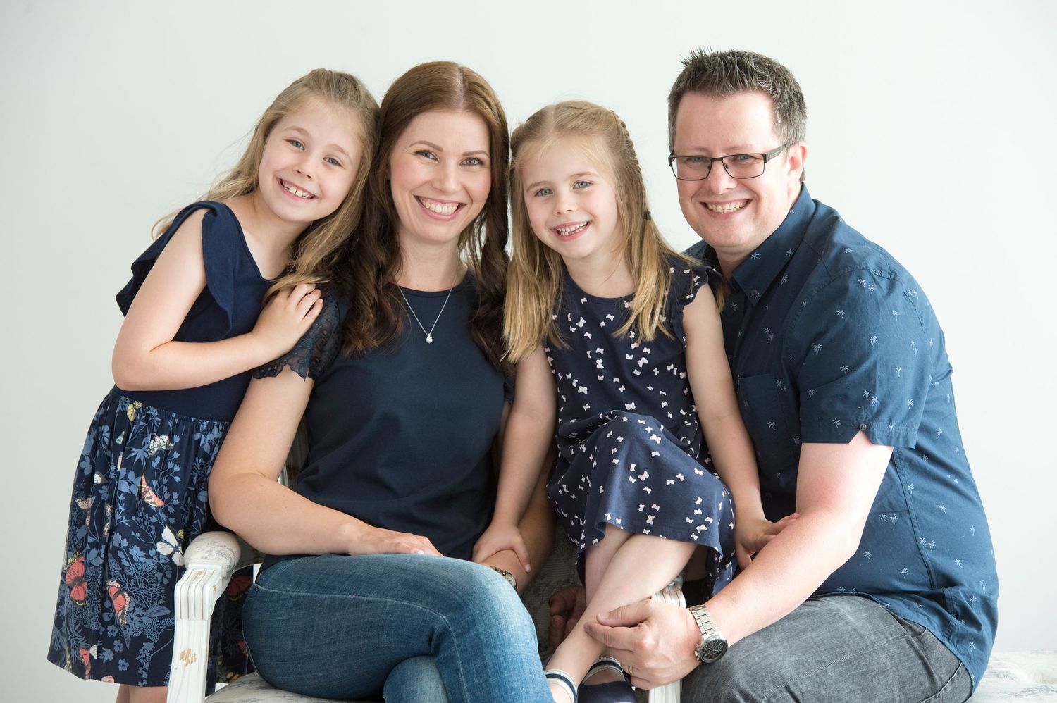 Studio portrait of a happy family of four wearing coordinated navy blue outfits against white background.