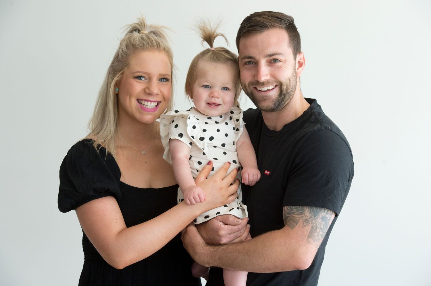 Family portrait with baby in polka dot outfit against white background.