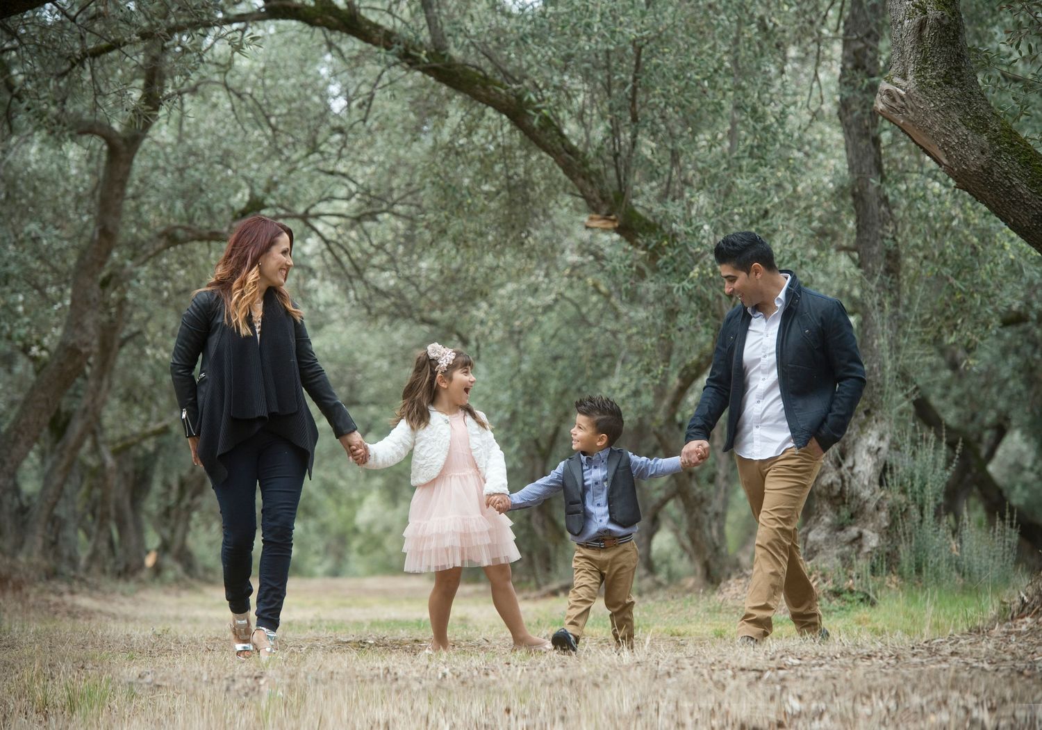 Family walking and holding hands together on wooded path during outdoor photo session.